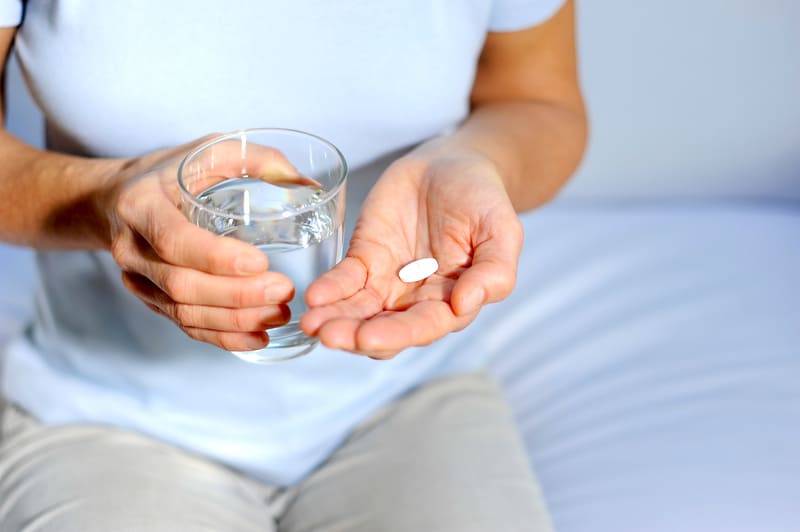 Behandlungen mit Tabletten - Frau mit Tabeltte und Wasserglas in der Hand